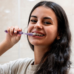 a teen with braces brushing her teeth